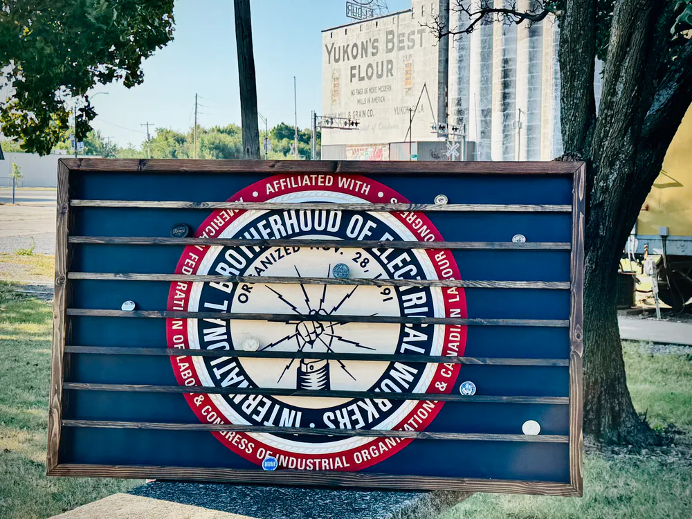 Oversized IBEW challenge coin display with a blue backing, wood frame, and coin shelves in front of Yukon’s Best Flour
