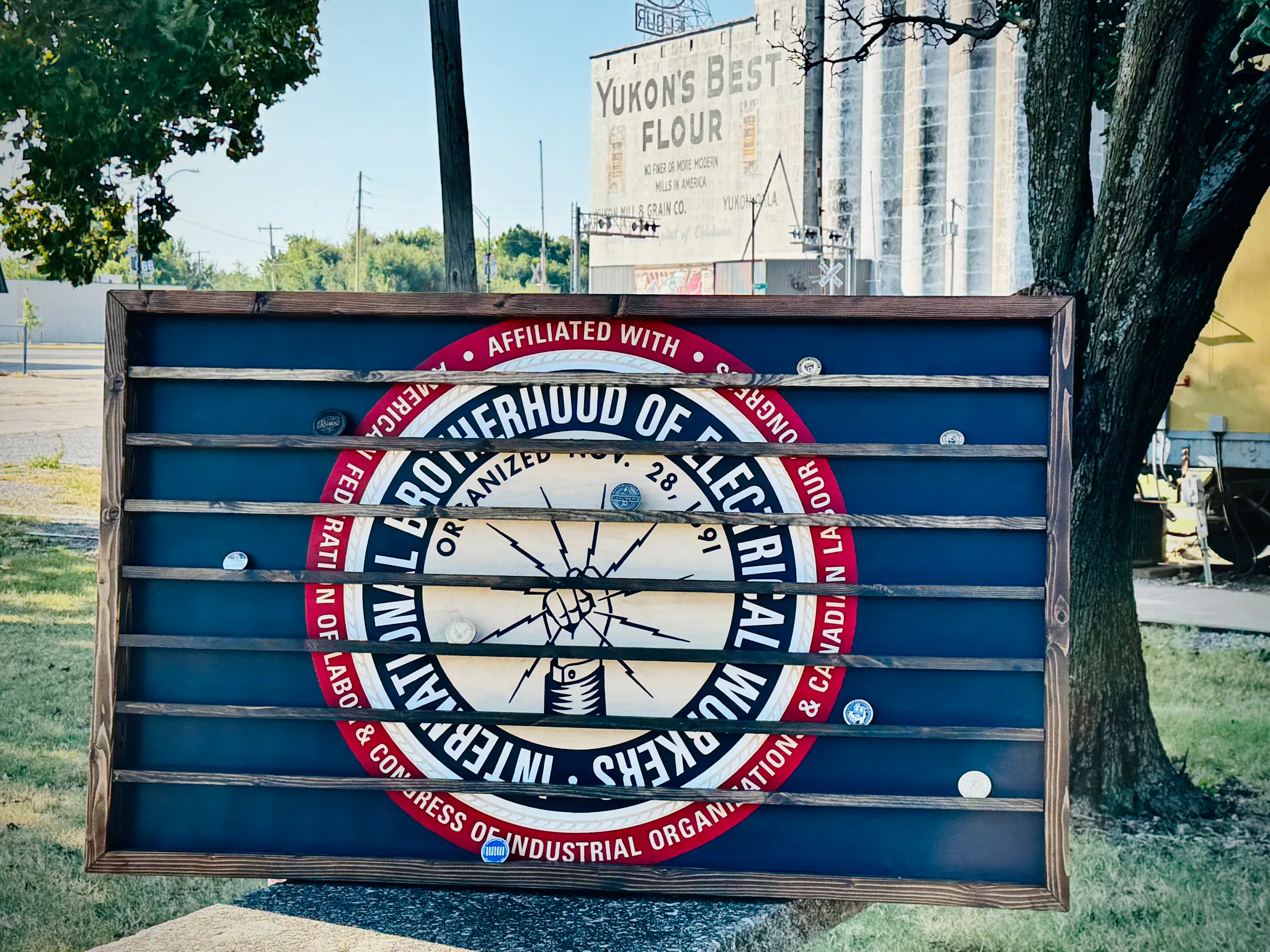 Oversized IBEW challenge coin display with a blue backing, wood frame, and coin shelves in front of Yukon’s Best Flour